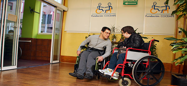 Dos usuarios charlan a la entrada de la residencia de Fundación COCEMFE en Madrid, financiada por el IRPF