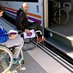 Dos personas con movilidad reducida frente a un tren de Cercanías con barreras