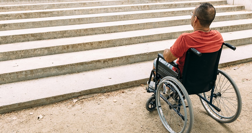 disabled person on wheelchair stopped in front of stairs who can't climb looking up for help, raising awareness of architectural barriers and accessibility issues for people with reduced mobility