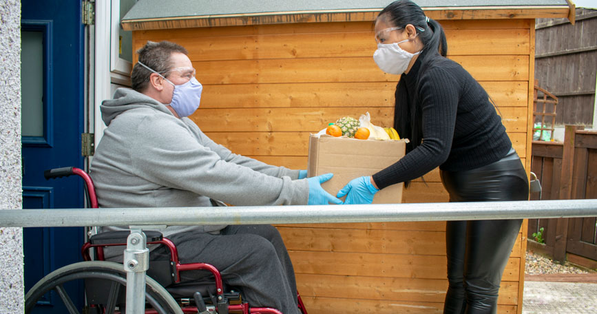 Una persona con movilidad reducida recibe una caja con alimentos en la entrada de su vivienda