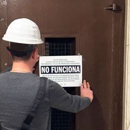 Un hombre coloca un cartel de 'No funciona' en un ascensor averiado.