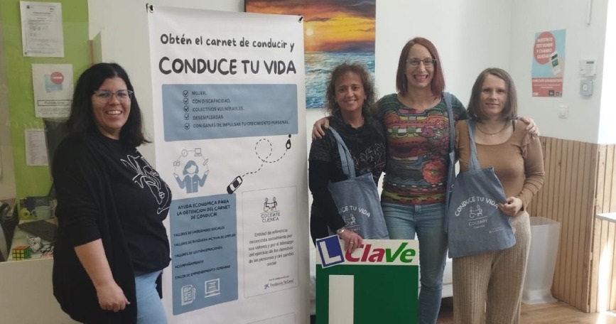 Mujeres participantes del programa Conduce tu Vida junto al roll-up de COCEMFE Cuenca en una autoescuela colaboradora