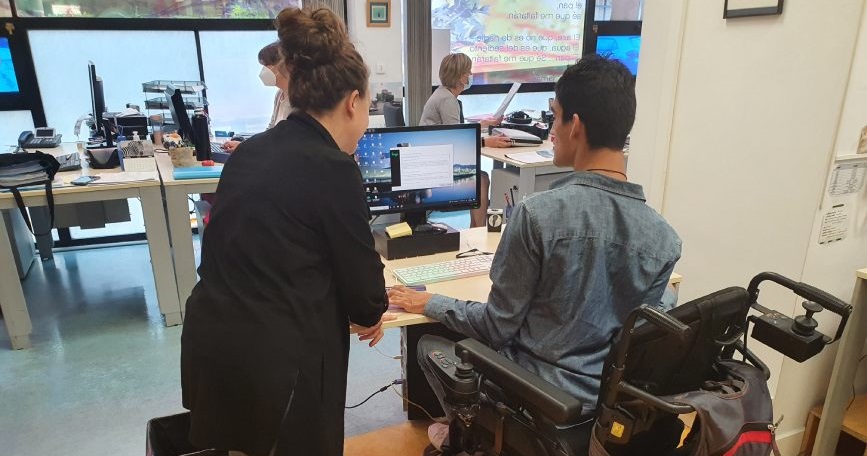 Técnica orienta a persona con discapacidad en silla de ruedas frente al ordenador