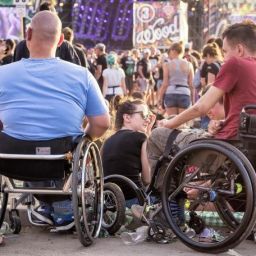 Personas en silla de ruedas disfrutando de un festival entre el público, con escenario y ambiente festivo de fondo.