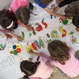 Grupo de niños pintando un mural colorido sobre inclusión y diversidad en una actividad educativa.