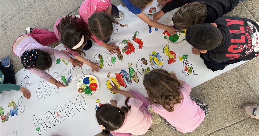 Grupo de niños pintando un mural colorido sobre inclusión y diversidad en una actividad educativa.