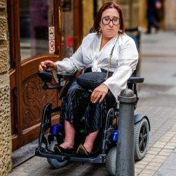 Barreras arquitectónicas en la vía pública en Madrid Mujer en silla de ruedas eléctrica frente a un bolardo y un escalón que impiden su paso en una calle de Madrid.