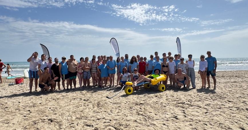 Más de 70 personas, incluyendo participantes con discapacidad, familiares y voluntariado, posan en la playa del Gurugú en la V Jornada Mediterráneo Accesible de COCEMFE Castelló y Asbumeca.