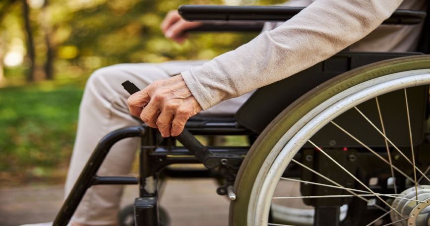 Mano de una persona mayor en silla de ruedas en un entorno natural.