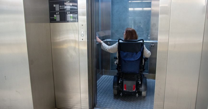 Mujer en silla de ruedas entra en un ascensor accesible, simbolizando la importancia de la accesibilidad y la vida independiente