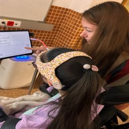 Educadora apoya a alumna con discapacidad mientras usa una tableta adaptada para comunicarse.