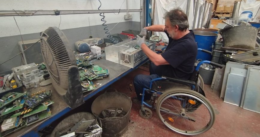 Hombre en silla de ruedas trabajando con componentes electrónicos en un taller adaptado de COCEMFE Castelló dentro del proyecto Sumando capacidades.