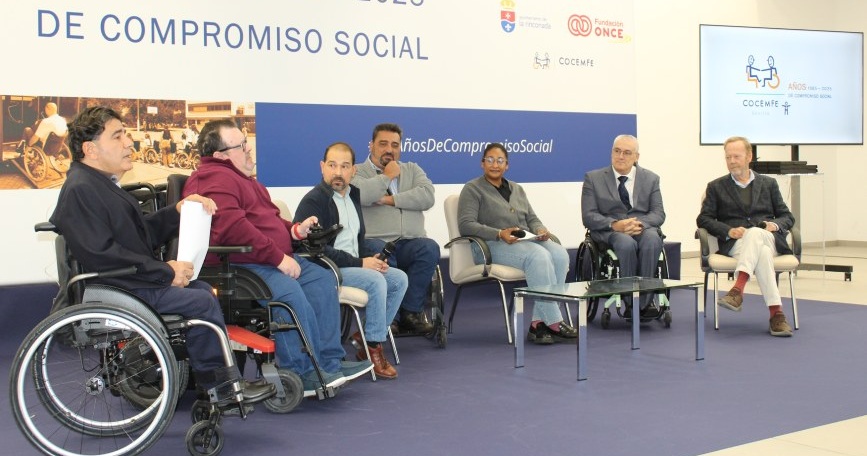 Personas participantes en una mesa de diálogo durante el 40º aniversario de COCEMFE Sevilla, con panel institucional de fondo.
