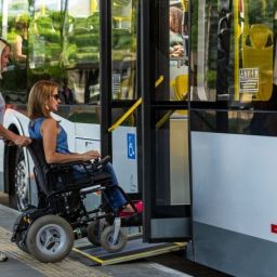 Mujer en silla de ruedas entrando a un autobús mediante una rampa asistida por una trabajadora.