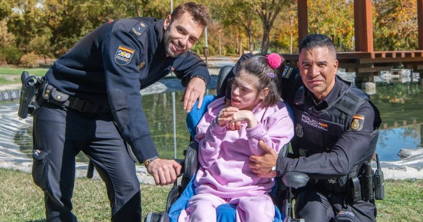 Dos agentes de Policía Nacional posan con una joven usuaria de silla de ruedas en un parque, en una actividad de sensibilización organizada por AMIFP.