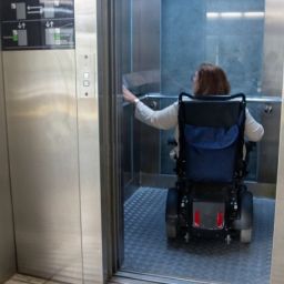 Mujer en silla de ruedas eléctrica entrando en un ascensor accesible.