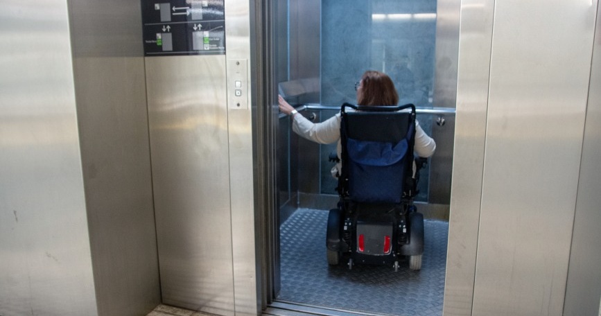 Mujer en silla de ruedas eléctrica entrando en un ascensor accesible.
