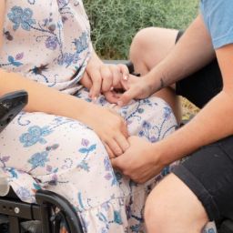 Encuentro afectivo entre dos personas, una de ellas usuaria de silla de ruedas Dos personas sentadas se toman de las manos, una de ellas usuaria de silla de ruedas, en un entorno exterior.