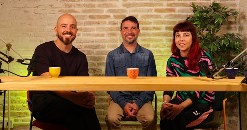 Tres personas participan en la grabación del podcast “Voces con FQ”, sentadas ante una mesa con micrófonos y tazas de colores en un estudio iluminado.