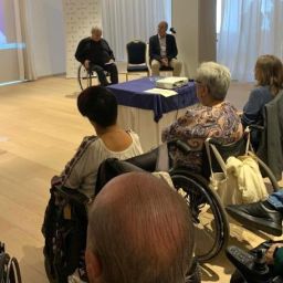 Ponente habla ante un público diverso, con varias personas en silla de ruedas, durante una jornada sobre inclusión.