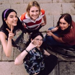 Jóvenes en un entorno inclusivo Cuatro jóvenes, incluida una usuaria de silla de ruedas, posan juntas en unas escaleras de piedra desde un plano cenital.