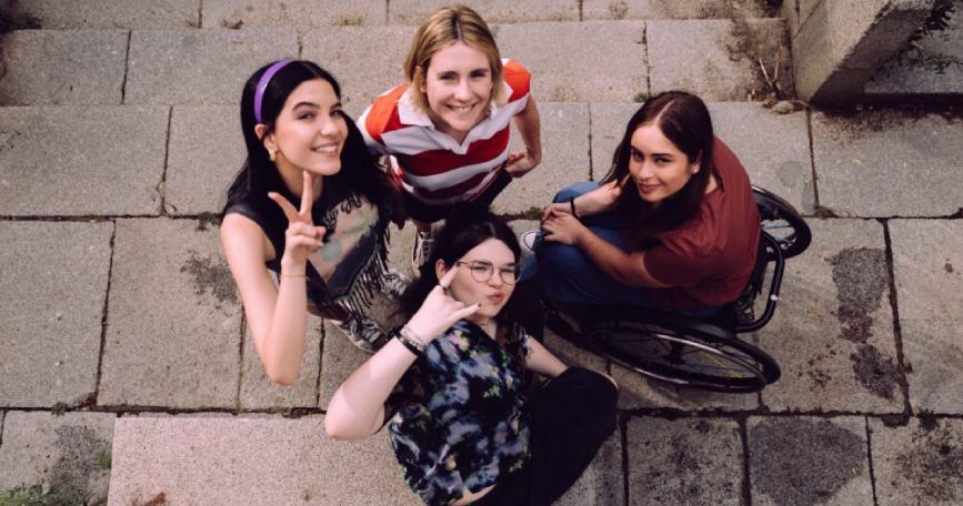 Cuatro jóvenes, incluida una usuaria de silla de ruedas, posan juntas en unas escaleras de piedra desde un plano cenital.