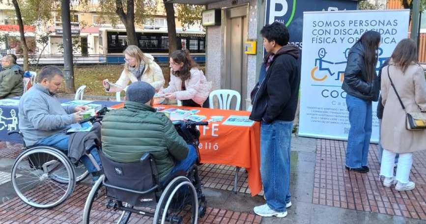 Mesa informativa de COCEMFE Castellón con personas usuarias y voluntariado en la plaza Borrull de Castelló de la Plana.