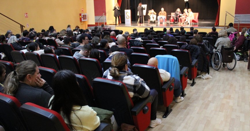 Auditorio lleno durante el acto institucional del Día de la Discapacidad en Sevilla, con panel de intervención e intérprete de lengua de signos en escena.
