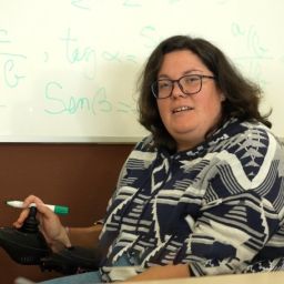 Mujer en silla de ruedas frente a una pizarra en un aula durante una actividad formativa.