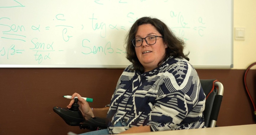 Mujer en silla de ruedas frente a una pizarra en un aula durante una actividad formativa.