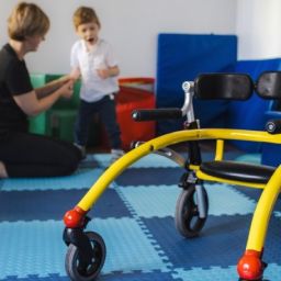 Atención temprana y movilidad infantil en entorno terapéutico Niño con discapacidad motora realizando una actividad de atención temprana junto a una profesional, con un andador adaptado en primer plano.