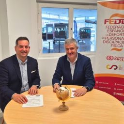 Representantes de la FEDDF y Rehatrans firmando un acuerdo de colaboración en una sala con vehículos adaptados al fondo.