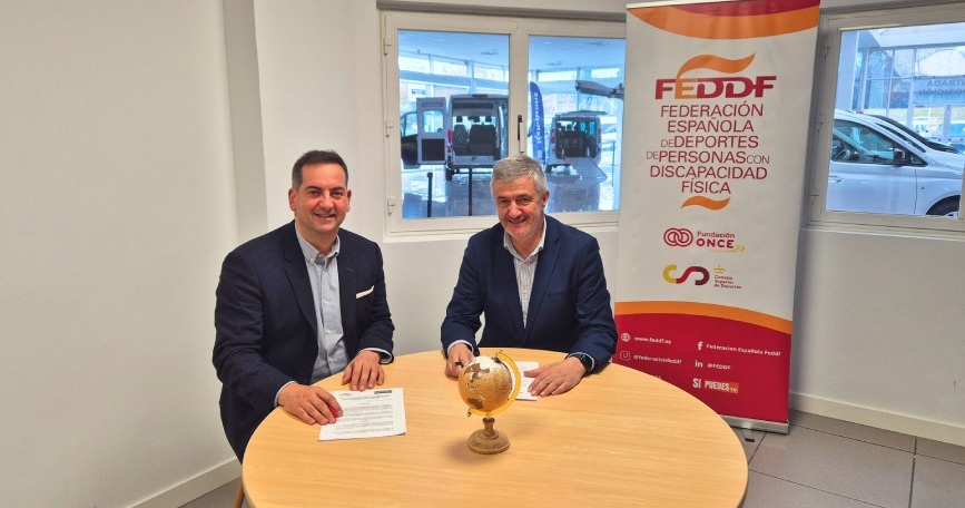 Representantes de la FEDDF y Rehatrans firmando un acuerdo de colaboración en una sala con vehículos adaptados al fondo.