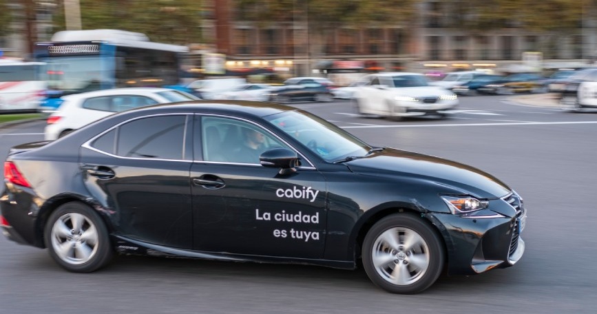 Coche de Cabify circulando por una avenida de Madrid con el logotipo de la empresa en la puerta.