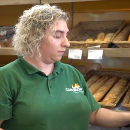 Empleo en comercio para personas con discapacidad Persona trabajadora usando un terminal de venta en una panadería con estanterías de pan al fondo.