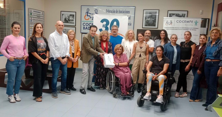 Fotografía de grupo en un encuentro de trabajo en COCEMFE, con personas de pie y una persona en silla de ruedas en el centro.