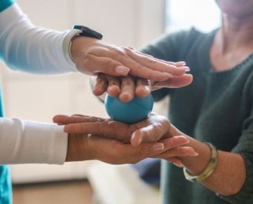 Apoyo profesional a personas con artritis Dos personas realizan un ejercicio con una pelota terapéutica durante una sesión de apoyo profesional para personas con artritis.