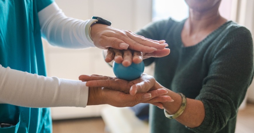 Dos personas realizan un ejercicio con una pelota terapéutica durante una sesión de apoyo profesional para personas con artritis.