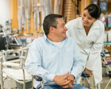 Persona usuaria de silla de ruedas recibe asesoramiento profesional sobre material ortoprotésico en un entorno sanitario accesible.