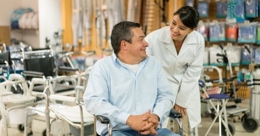 Persona usuaria de silla de ruedas recibe asesoramiento profesional sobre material ortoprotésico en un entorno sanitario accesible.