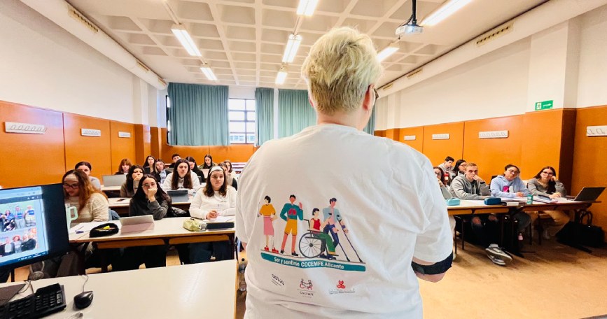 Ponente de COCEMFE Alicante imparte una charla a estudiantes de Trabajo Social en un aula de la Universidad de Alicante.
