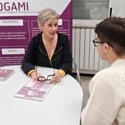 Profesional de COGAMI ofrece asesoramiento a un joven sobre discapacidad en un punto informativo.