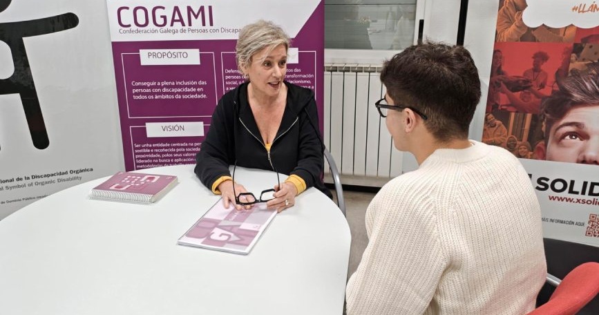 Profesional de COGAMI ofrece asesoramiento a un joven sobre discapacidad en un punto informativo.