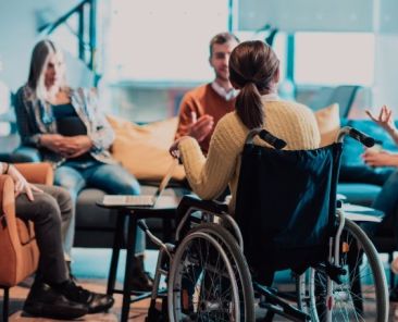 Grupo de profesionales dialoga en una sesión participativa sobre educación inclusiva, con una persona usuaria de silla de ruedas en el centro del grupo.