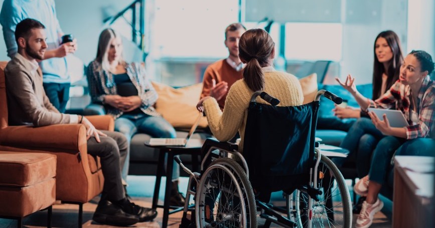 Grupo de profesionales dialoga en una sesión participativa sobre educación inclusiva, con una persona usuaria de silla de ruedas en el centro del grupo.