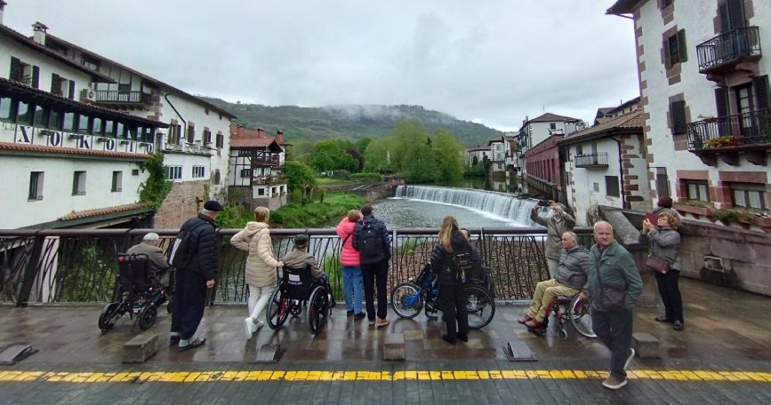 Grupo de personas con discapacidad observando un río desde un puente accesible durante el Programa de Vacaciones de COCEMFE