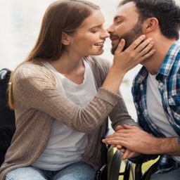 Mujer usuaria de silla de ruedas comparte un momento de afecto con su pareja en un entorno natural.