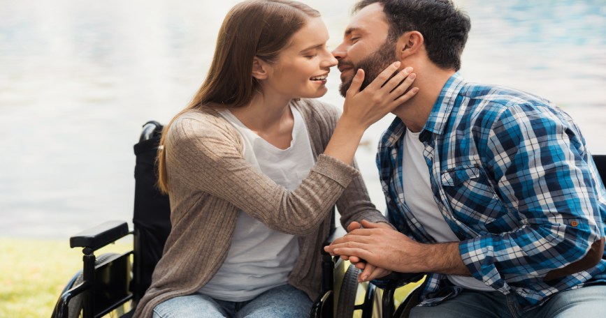 Mujer usuaria de silla de ruedas comparte un momento de afecto con su pareja en un entorno natural.