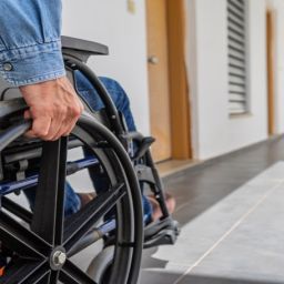 Persona usuaria de silla de ruedas desplazándose por el interior de un edificio residencial, representando la necesidad de accesibilidad en viviendas.