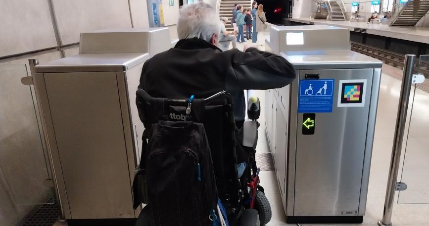 Persona usuaria de silla de ruedas pasando por una canceladora accesible en una estación de tren de Euskotren.